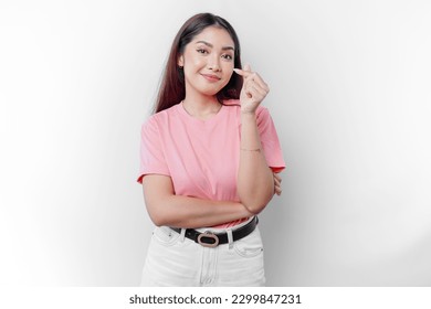 A happy young Asian woman wearing a pink t-shirt feels romantic shapes heart gesture expressing tender feelings  - Powered by Shutterstock