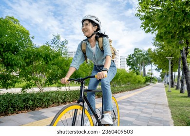 Happy young Asian woman while riding a bicycle in a city park. She smiled using the bicycle of transportation. Environmentally friendly concept. - Powered by Shutterstock