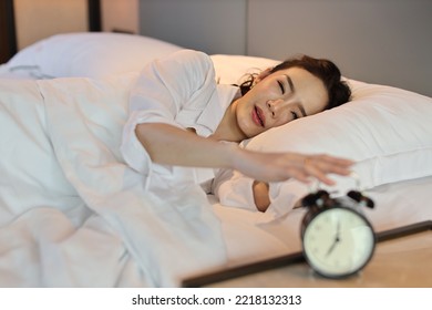 Happy Young Asian Woman In White Lingerie Lying In Bed, Wake Up Late And Overslept Morning, Trying To Stop Alarm Clock. Cute Girl Look Comfortable, Need More Sleep. Difficult Morning Get Up Concept 