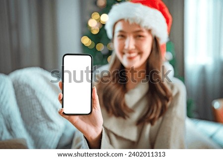 Happy young asian women wearing santa hat and show smartphone mock up with blank screen in Christmas time. Put your text in empty space.