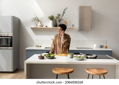 Happy Young Attractive African American Woman In Glasses Holding Pleasant Cellphone Call Conversation, Communicating With Friends Inviting For Domestic Party, Distracted From Preparing Food In Kitchen