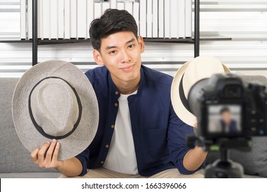 Happy young attractive Asian male blogger or vlogger present hat on live streaming, broadcast with internet subscribers. Social media influence people, content maker, e-commerce, Work at home concept.