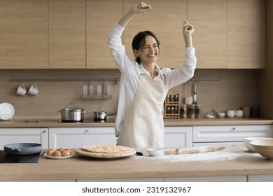 Happy young attractive woman dancing in kitchen while cooking homemade pizza, female in apron moving to favourite music, feels carefree, enjoy pastries preparation on weekend at home. Culinary, hobby - Powered by Shutterstock