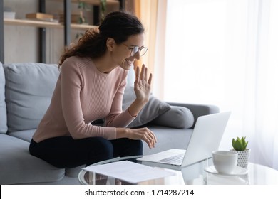 Happy young attractive woman in glasses looking at laptop screen, waving hands, holding video call with friends from home. Smiling pretty millennial teacher making hello hi gesture, welcoming clients. - Shutterstock ID 1714287214
