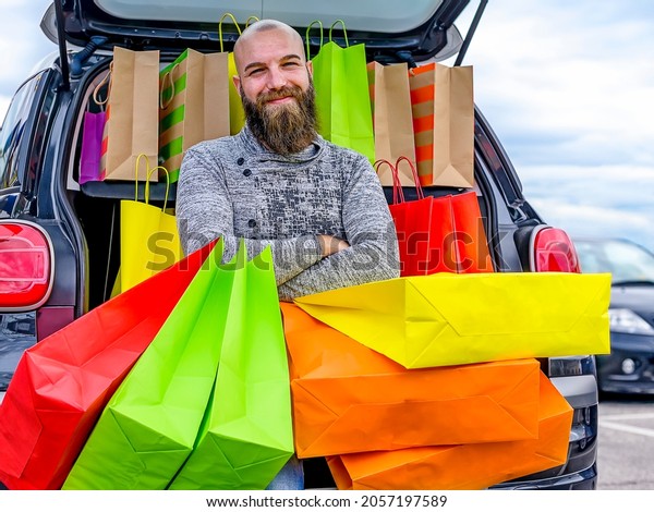 Happy young\
bald bearded man with car trunk full of colorful bags after a day\
of Christmas shopping - Satisfied boy after buying gifts for his\
girlfriend - sale and consumerism\
concept