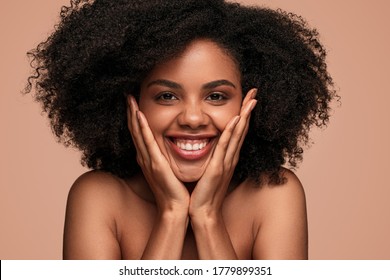 Happy Young Bare Shouldered Black Female With Smooth Skin Touching Face And Looking At Camera On Orange Background