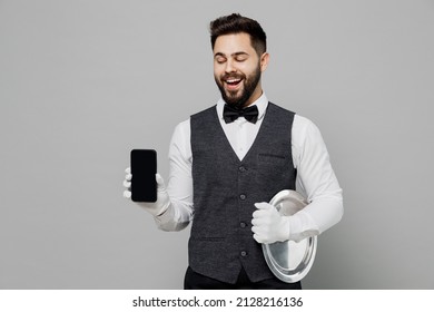 Happy Young Barista Male Waiter Butler Man 20s Wear White Shirt Vest Elegant Uniform Work At Cafe Hold Mobile Phone With Blank Screen Isolated On Plain Grey Background. Restaurant Employee Concept.