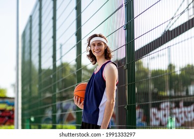 Happy young basketballer in sportswear posing and smiling at camera in outdoor game court, copy space. Handsome millennial sportsman with ball ready to participate in tournament - Powered by Shutterstock