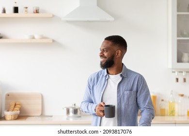 Happy young bearded african american guy with cup of coffee in hand in minimalist kitchen interior looks at empty space. Good morning, ad, great offer, positive lifestyle due self-isolation covid-19 - Powered by Shutterstock