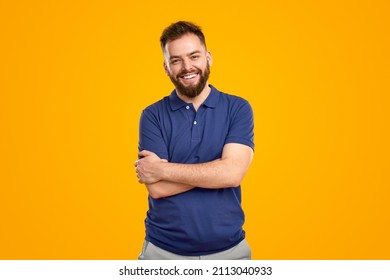 Happy Young Bearded Guy In Blue Polo Shirt Smiling And Looking At Camera While Standing Against Bright Yellow Background With Crossed Arms