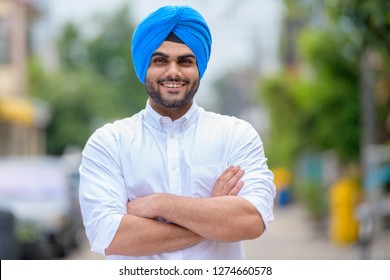 Happy young bearded Indian Sikh man smiling outdoors