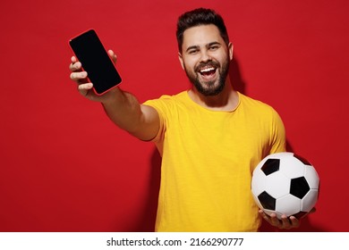 Happy Young Bearded Man Football Fan In Yellow T-shirt Support Favorite Team Hold Soccer Ball Mobile Cell Phone With Blank Screen Workspace Area Isolated On Plain Dark Red Background Studio Portrait