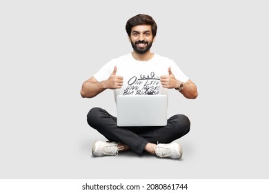 Happy Young Bearded Man Sitting With Crossed Legs Using Laptop With Thumbs Up On White Background - Pakistani Indian South Asian