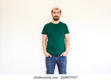 Happy Young Bearded Muslim Man Isolated On White Background. Modern  Muslim Guy Wearing Green T Shirt, Jeans And Taqiyah (cap).