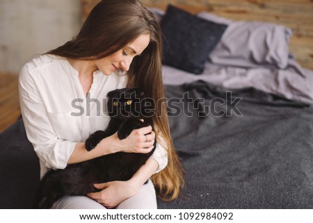Happy young beautiful caucasian woman smiling and holding a black cat. Playing with pet at home. Love, coziness, leisure, animal protection concept. Scottish fold breed.
