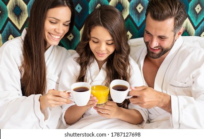 Happy Young Beautiful Family In Bathrobes Are Taking Morning Breakfast In A Luxury Hotel Room. Service In The Room. Vacation And Trip