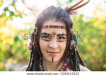 Happy young beautiful girl in image of native American smiles and looks at camera in sunny summer day