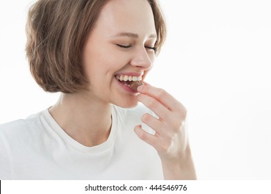 Happy Young Beautiful Lady Eating Chocolate And Smiling. Big Lips. Girl Tasting Sweet Chocolate, Short Haired Young Woman With Natural Make Up  Having Fun And Eating Chocolate Candy 