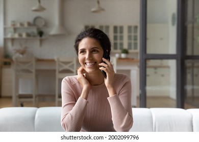 Happy Young Beautiful Latin Woman Sitting On Comfortable Sofa, Involved In Pleasant Smartphone Conversation, Talking With Friends Or Family, Sharing Good Life News, Distant Communication Concept.