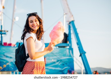 Happy young beautiful woman eating cotton candy at fairground