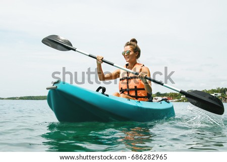 Happy young and beautiful woman kayaking in on the lake