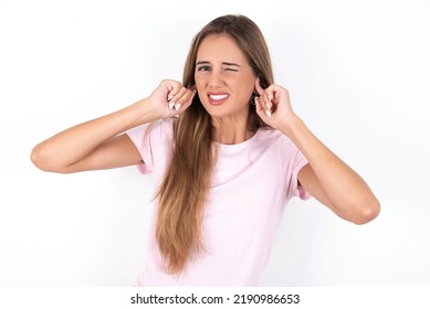 Happy Young Beautiful Woman Wearing Pink T-shirt Over White Background Ignores Loud Music And Plugs Ears With Fingers Asks To Turn Off Sound