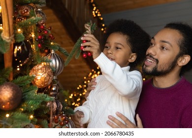 Happy Young Biracial Father And Small Son Have Fun Decorate Christmas Tree At Home Together. Smiling Loving African American Dad Help Little Boy Child With New Year Winter Holiday Preparation.