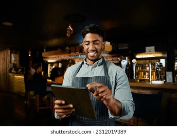 Happy young biracial man in apron pointing at digital tablet while working as waiter in bar - Powered by Shutterstock