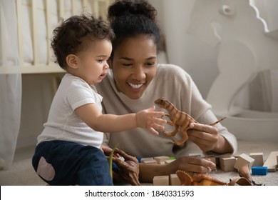 Happy young biracial mom lying on floor play with small curious ethnic baby infant at home. Smiling loving African American mother engaged in funny activity with small infant child. Childcare concept.