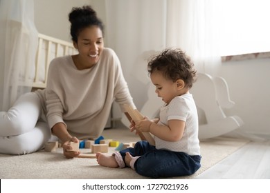 Happy Young Biracial Mother Sit On Floor Play With Building Blocks Bricks With Little Infant Toddler, Smiling African American Mom Engaged In Learning Activity With Small Baby Child At Home