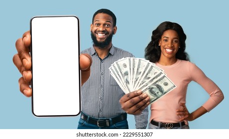 Happy young black couple in casual showing bunch of cash and modern cell phone with white blank screen, man and woman gambling on Internet, blue studio background, mockup, collage
