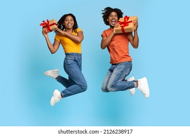 Happy young black couple holding presents and jumping up over blue studio background, cheerful millennial african american man and woman celebrating anniversary, exchanging gifts - Powered by Shutterstock