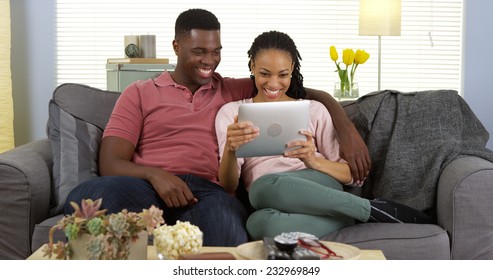 Happy Young Black Couple Laughing And Using Tablet Computer On Sofa