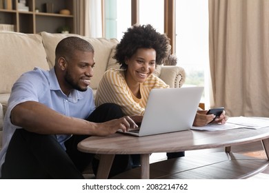 Happy young Black couple using laptop, looking at screen, smiling, laughing, getting good news. Husband and wife using online banking app on computer, paying bills, insurance mortgage fees on internet - Powered by Shutterstock