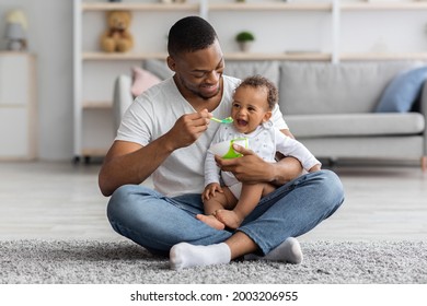 Happy Young Black Dad Spoon Feeding His Cute Adorable Baby Son At Home, Loving African American Father Taking Care About Little Male Infant Child Enjoying Paternity Leave Time, Free Space