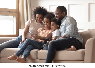 Happy Young Black Family With Preschooler Children Have Fun Relax Together On Sofa At Home Watching Video On Tablet, Smiling Parents Enjoy Spending Time With Little Kids Rest On Couch Using Pad