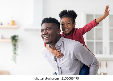 Happy Young Black Father Piggybacking His Pretty Little Daughter, Joyful African American Daddy And Kid Having Fun Together At Home, Looking At Copy Space And Smiling, Panorama