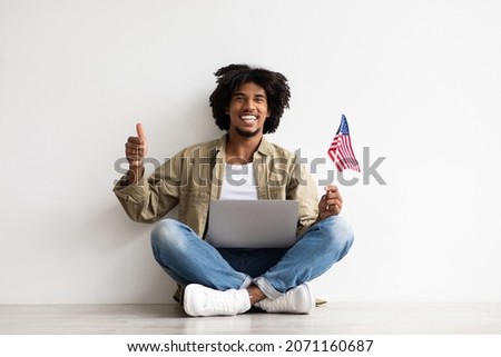 Happy Young Black Guy Sitting On Floor With Laptop And USA American Flag And Showing Thumb Up At Camera, Cheerful African Man Recommending Online Language Courses Or Internet Website, Copy Space