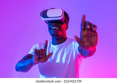 Happy young black guy in VR glasses exploring cyberspace, touching imaginary screen, playing virtual reality game in neon light. Positive African American man experiencing contemporary technologies - Shutterstock ID 2167421739