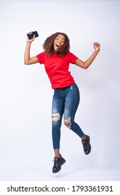 A Happy Young Black Lady Jumping In Excitement And Holding A Phone