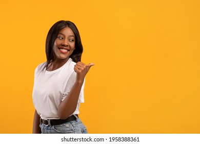 Happy young black lady pointing with thumb up at copy space over yellow studio background. Excited african american woman showing advertisement, indicating aside and smiling