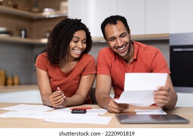 Happy Young Black Lady In Red T-shirt Shows Documents To Guy With Computer At Kitchen Interior. Great News, Bill Payment, Home Bookkeeping, Taxes Together, Household Chores, End Of Mortgage And Credit