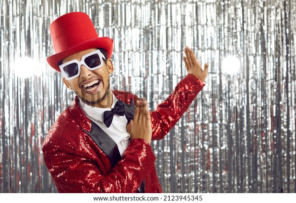 Happy\
young black man in red disco jacket dance on glitter background.\
Smiling African American entertainer or showman have fun on party\
or celebration in nightclub. Entertainment\
concept.