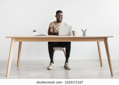Happy young black man using laptop computer for online work at table in home office, free space. Cool African American guy having remote job, freelancing on web. Modern business concept - Shutterstock ID 2103171167