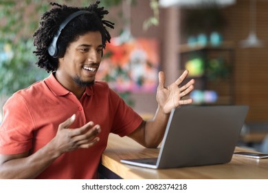 Happy Young Black Man Wearing Wireless Headphones Making Video Call With Laptop While Sitting At Table In Cafe, Cheerful African American Guy Having Online Meeting, Enjoying Virtual Communication