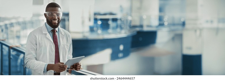 Happy young black man in workwear and protective glasses medical scientist with using digital tablet, analyzing data, posing at workplace, panorama with copy space. Jobs and occupations concept - Powered by Shutterstock