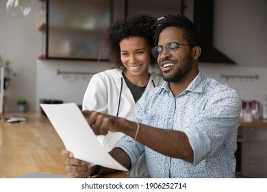 Happy young black married couple reading paper letter about financial reward at kitchen. Smiling satisfied afro american husband wife discuss good conditions of loan mortgage proposal received by mail