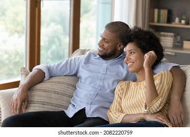 Happy Young Black Married Couple Relaxing On Couch At Home, Looking At Window Away, Talking, Dreaming On Future Family, Thinking Over House Buying, Planning Mortgage, Apartment Rent