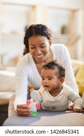 Happy Young Black Mother Showing Cute Toy For Teething To Excited Baby Boy On Sofa, Infant Exploring World Concept