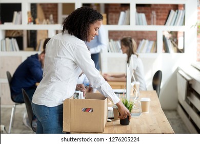 Happy young black newcomer newbie unpacking box with belongings at workplace on first working day concept, smiling african american new hired worker employee intern settling on work desk in office - Powered by Shutterstock